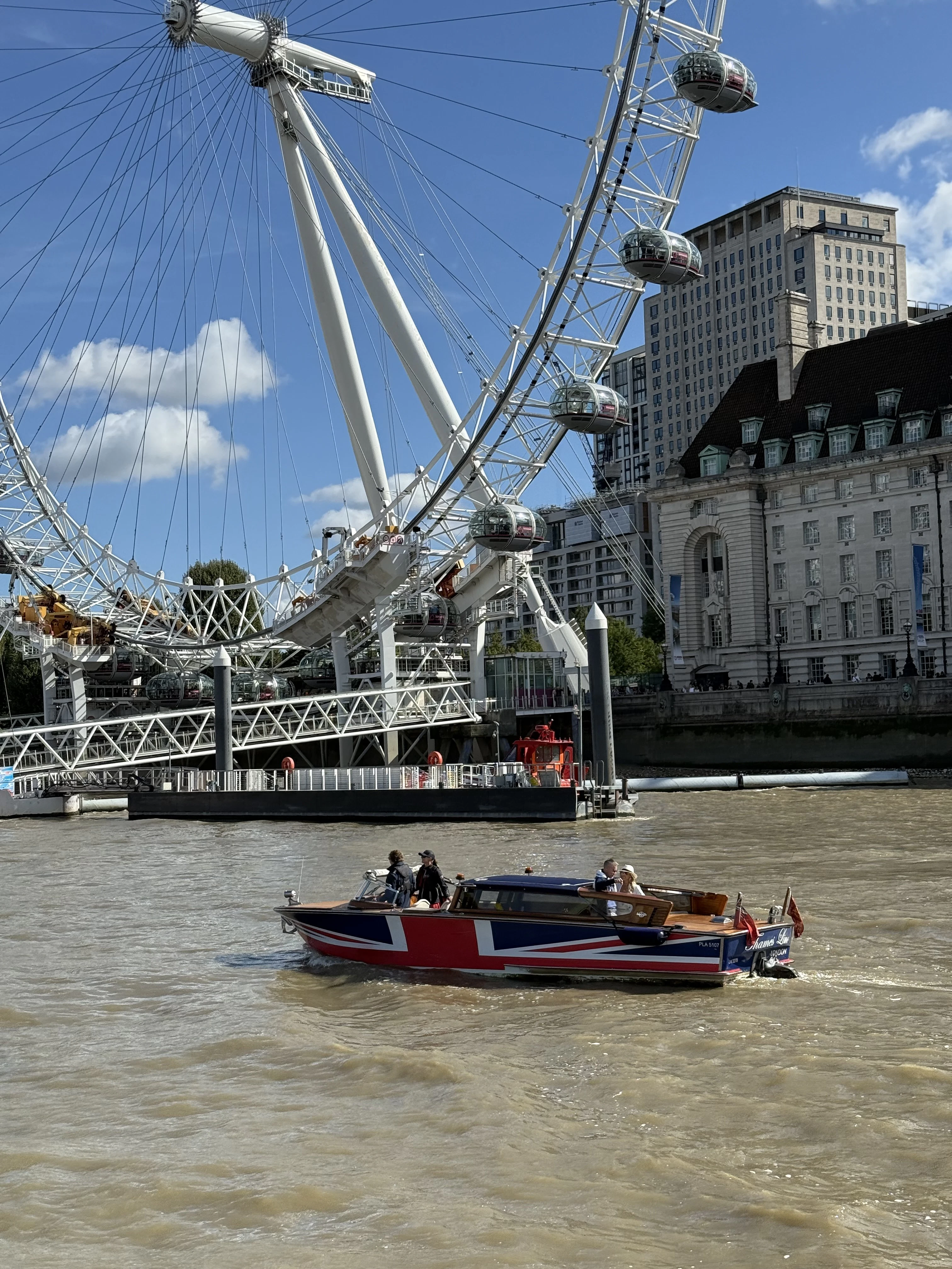 River boat decorated with Union Jack sailing on the Thames below the London Eye