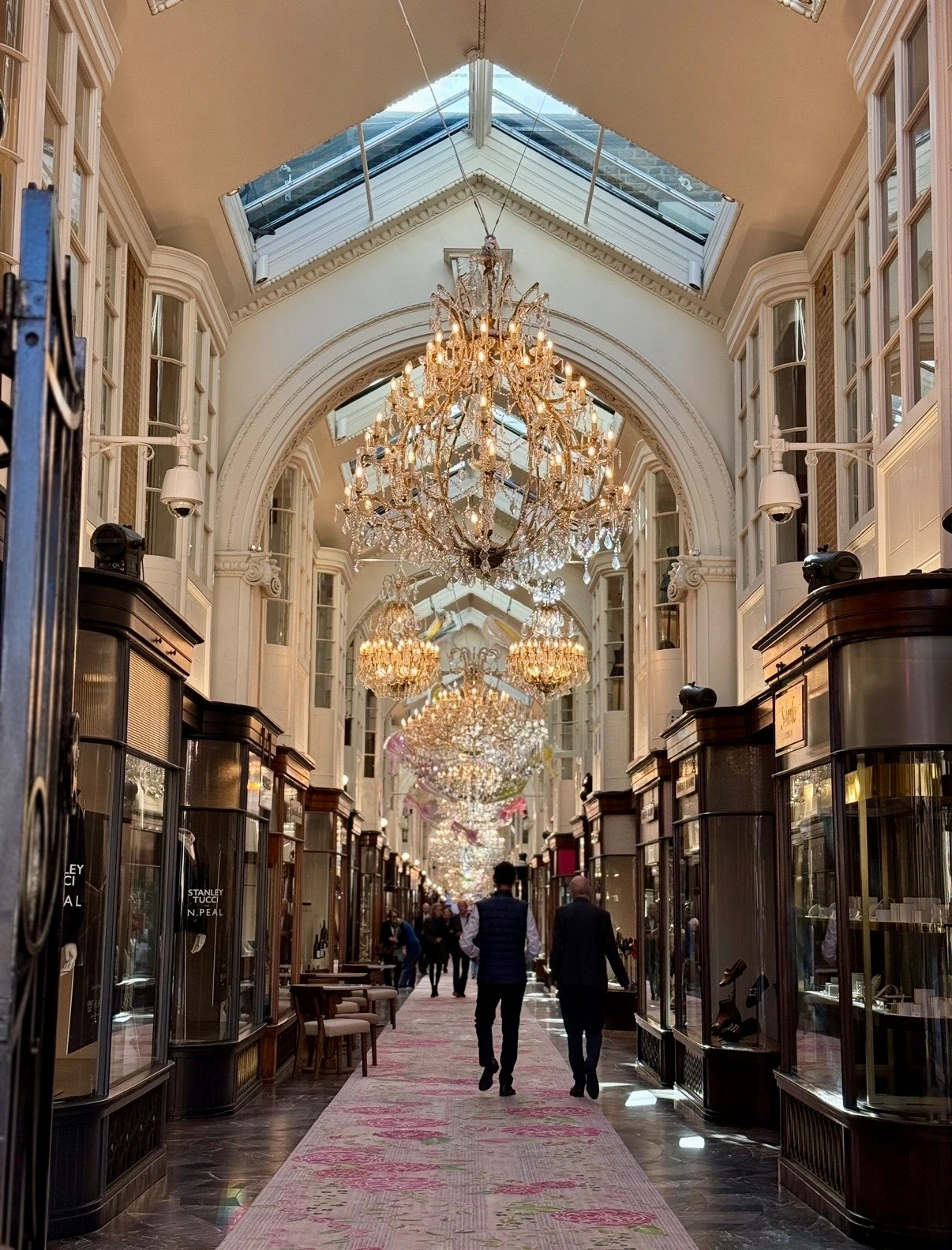 People walking down a high street shopping arcade with crystal chandeliers above