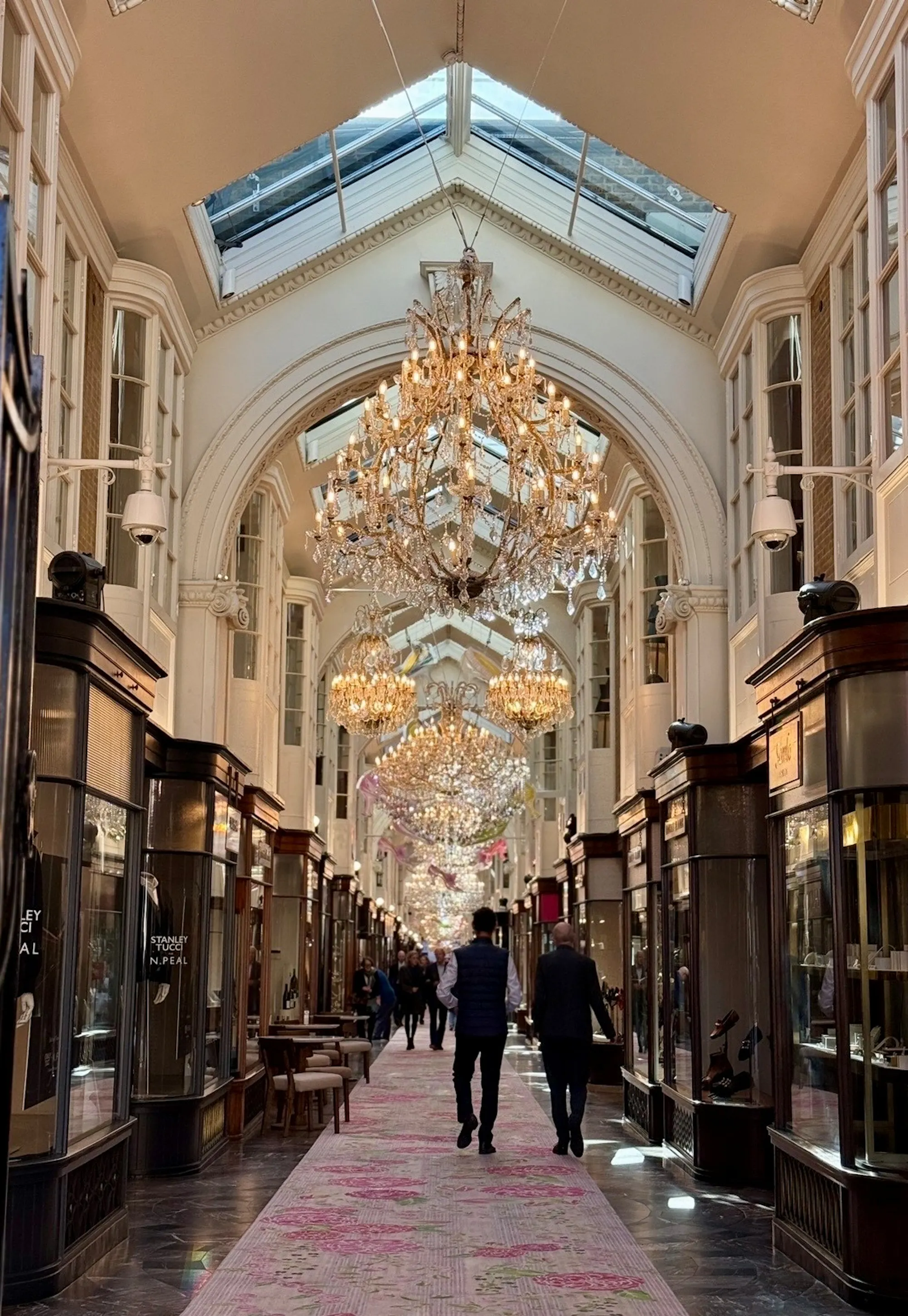 People walking down a high street shopping arcade with crystal chandeliers above