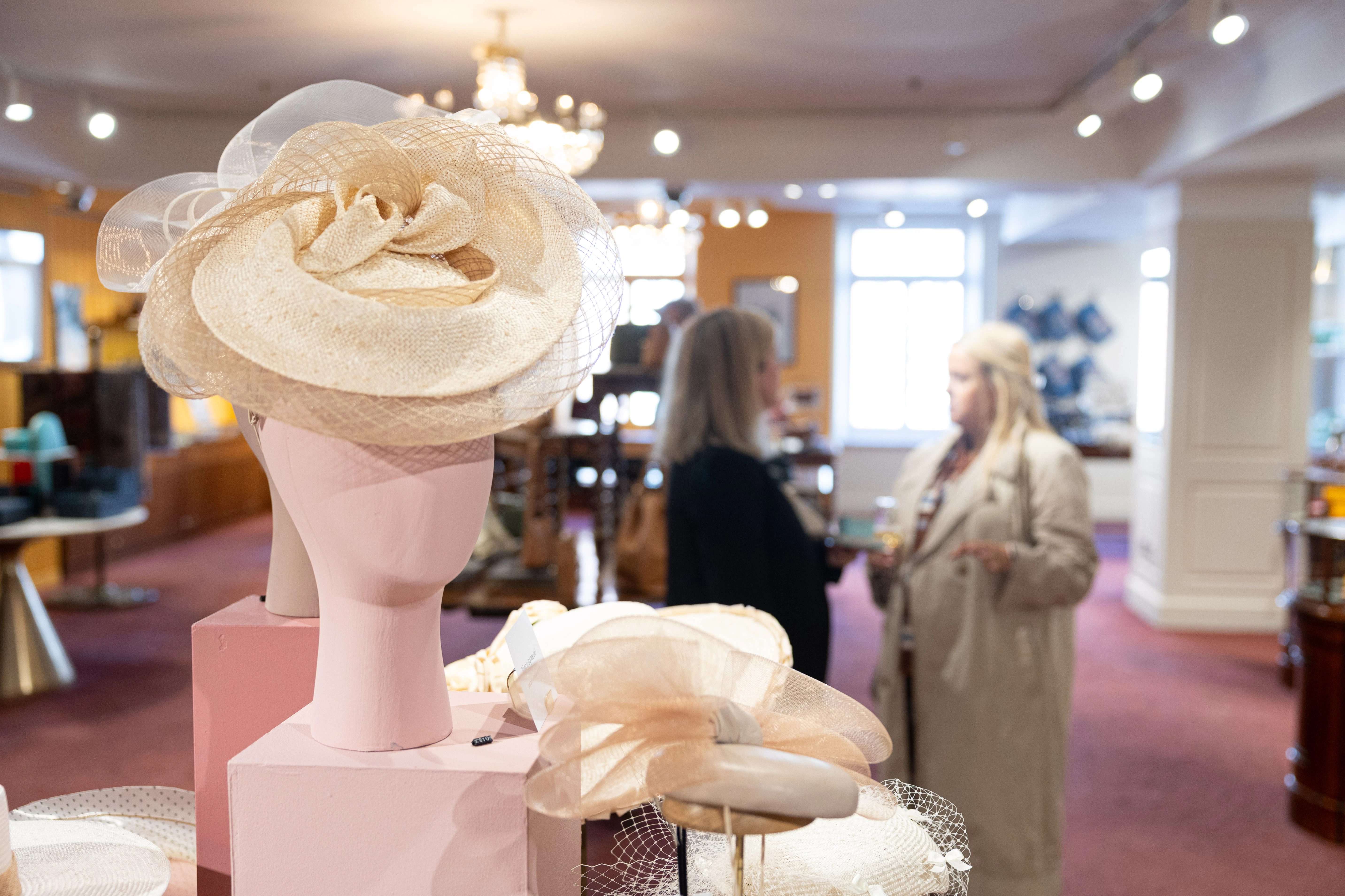 A beige sinamay fascinator featuring mesh loops and a wide brim, on display alongside other millinery hats.