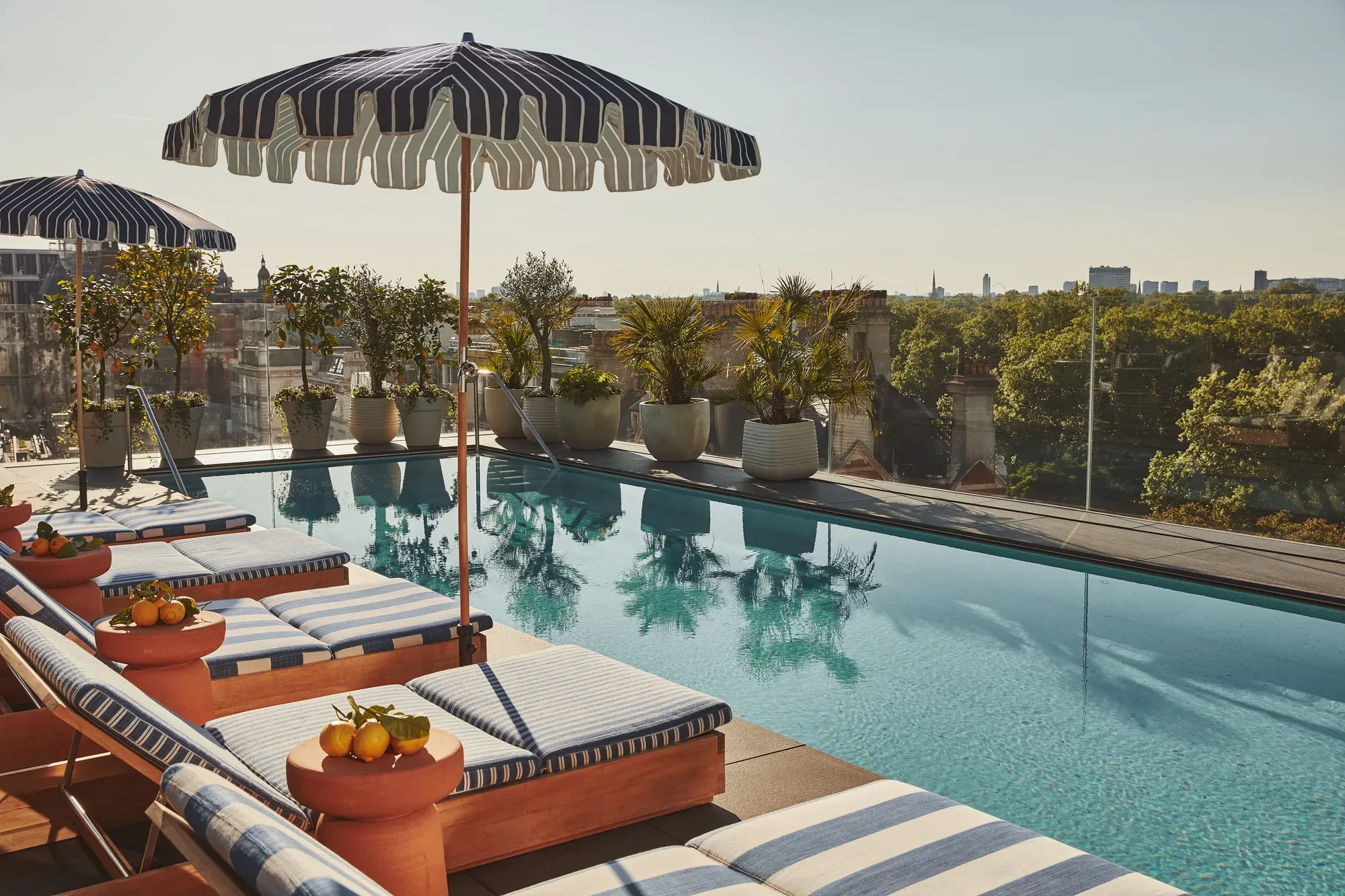 A corner view of the luxury outdoor swimming pool at The Berkeley hotel in London on a sunny day, lined with sun loungers.