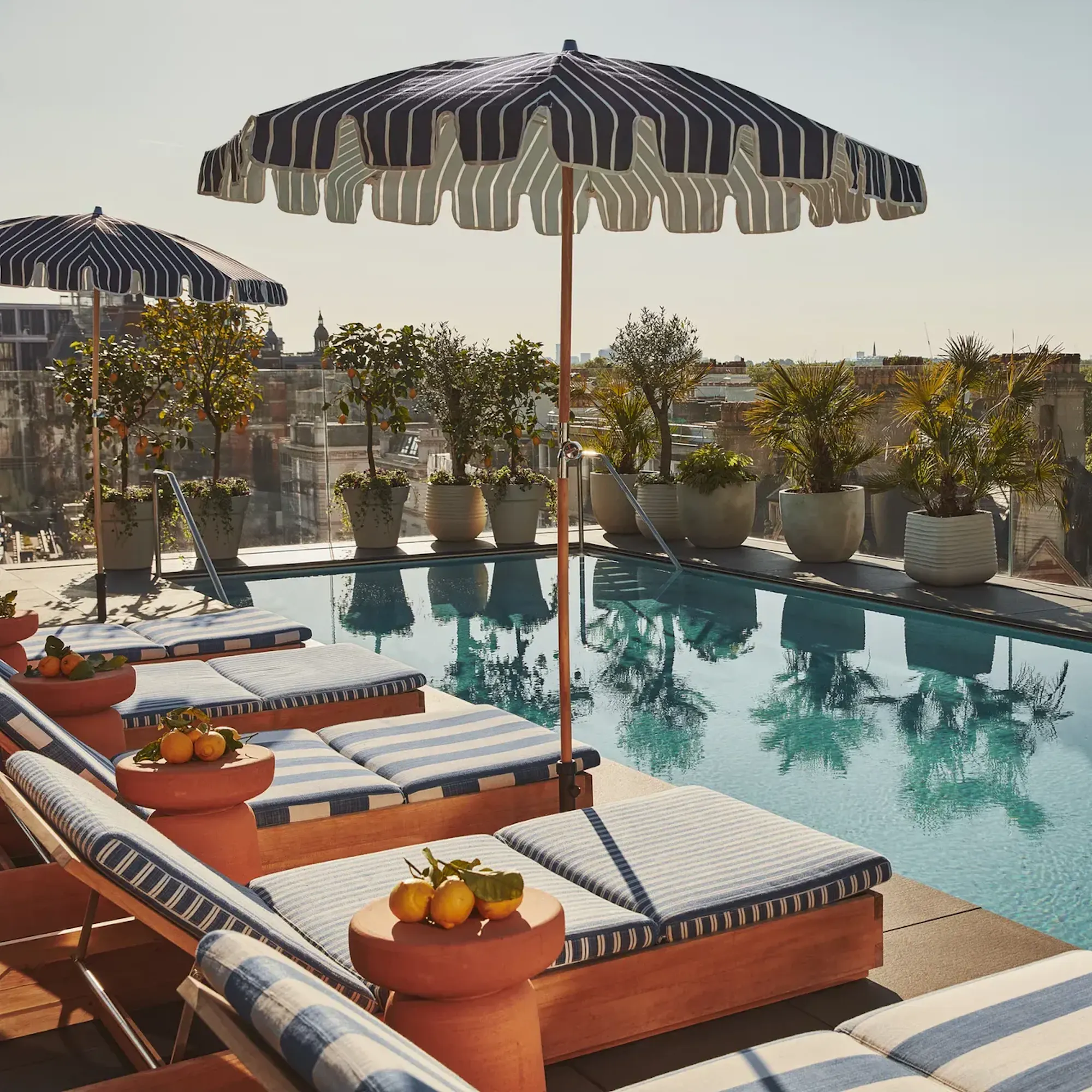 A corner view of the luxury outdoor swimming pool at The Berkeley hotel in London on a sunny day, lined with sun loungers.