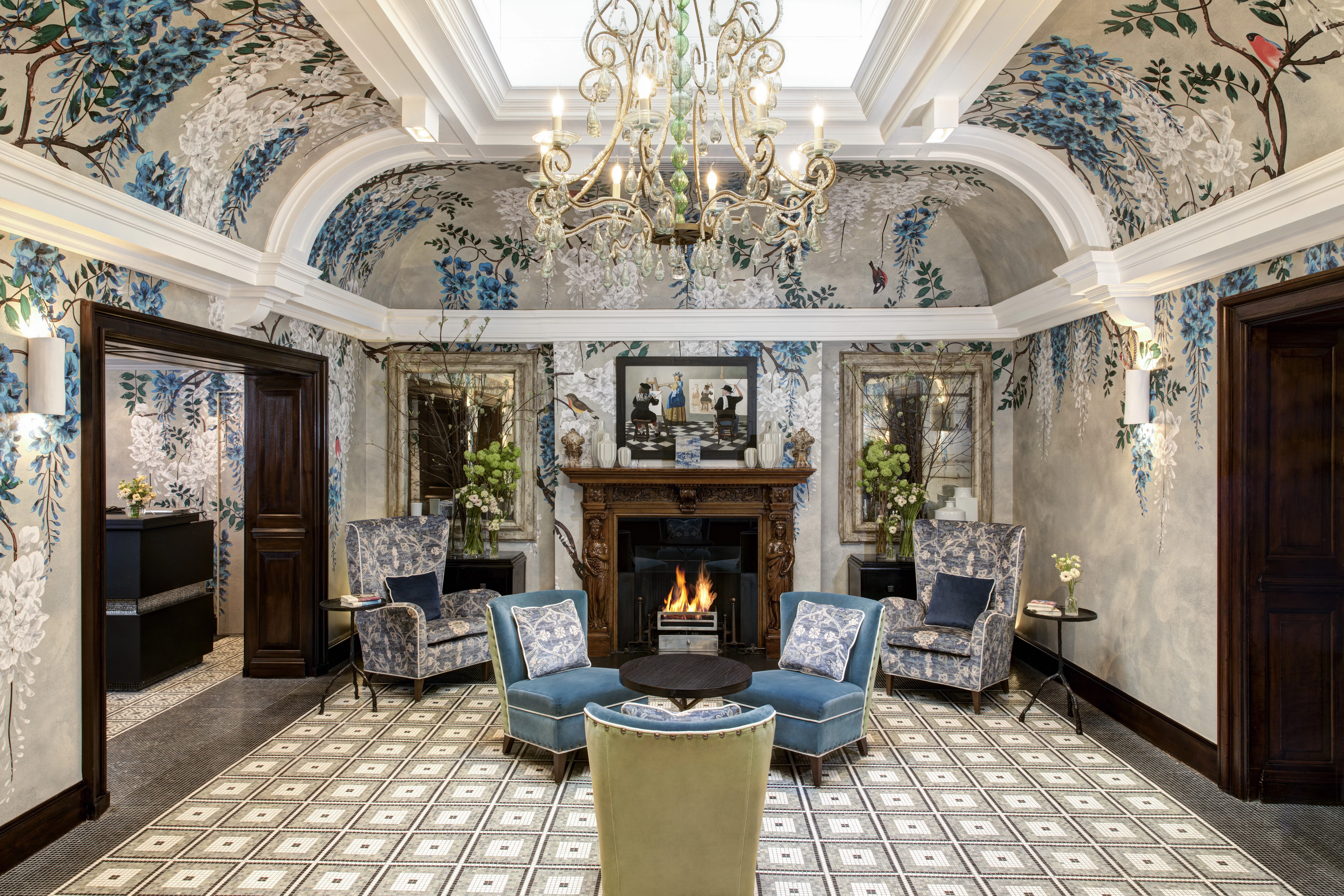 The luxury lobby interior at Brown's Hotel in London with blue upholstered seating, a fireplace, and a crystal chandelier.