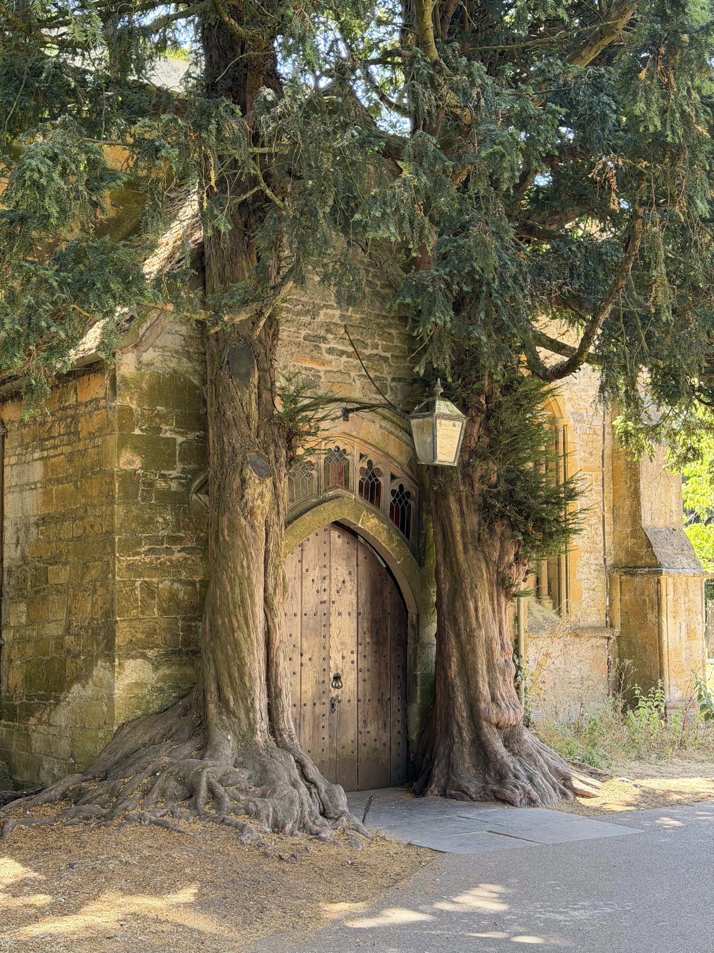 Wooden church door flanked by ancient trees, inspiration for Tolkien's Doors of Moria in Stow-on-the-Wold.