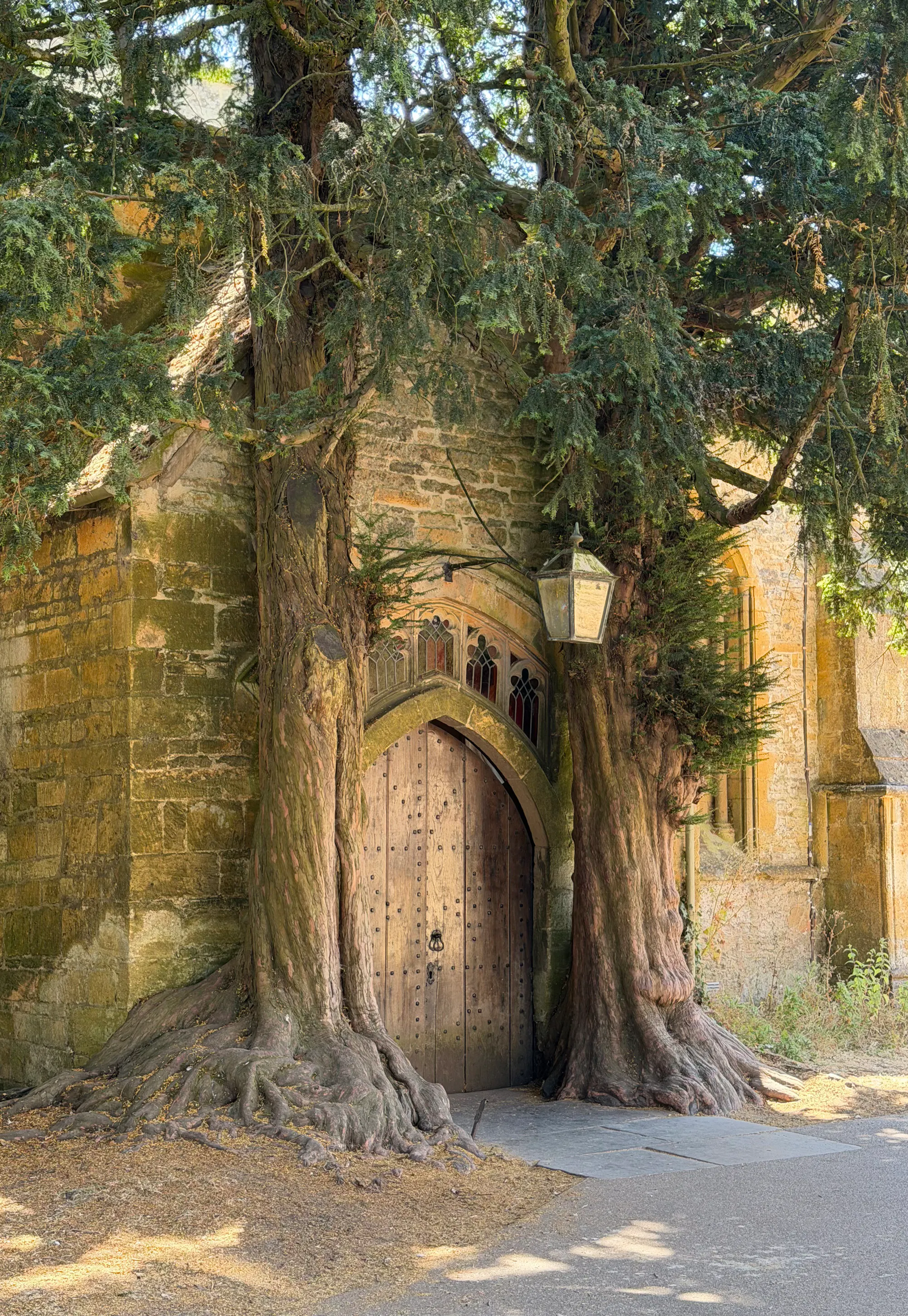 Wooden church door flanked by ancient trees, inspiration for Tolkien's Doors of Moria in Stow-on-the-Wold.