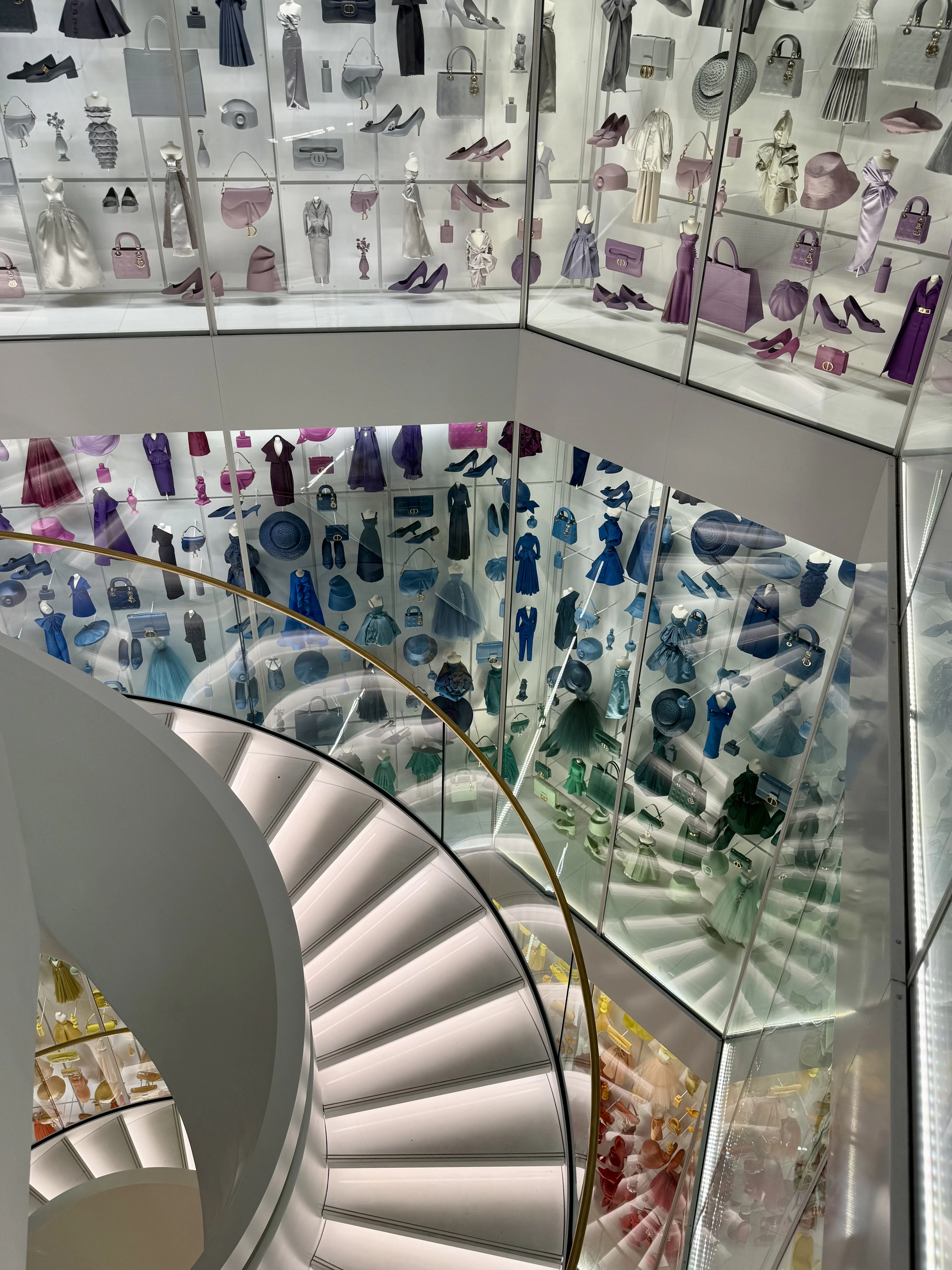 Spiral staircase surrounded by a rainbow-colored wall of Dior dresses, bags, and accessories in Paris.