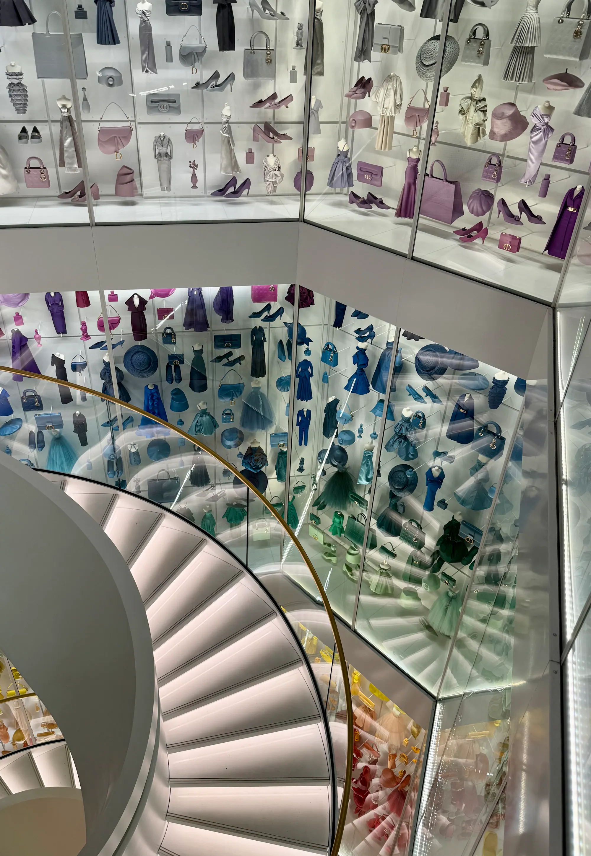 Spiral staircase surrounded by a rainbow-colored wall of Dior dresses, bags, and accessories in Paris.
