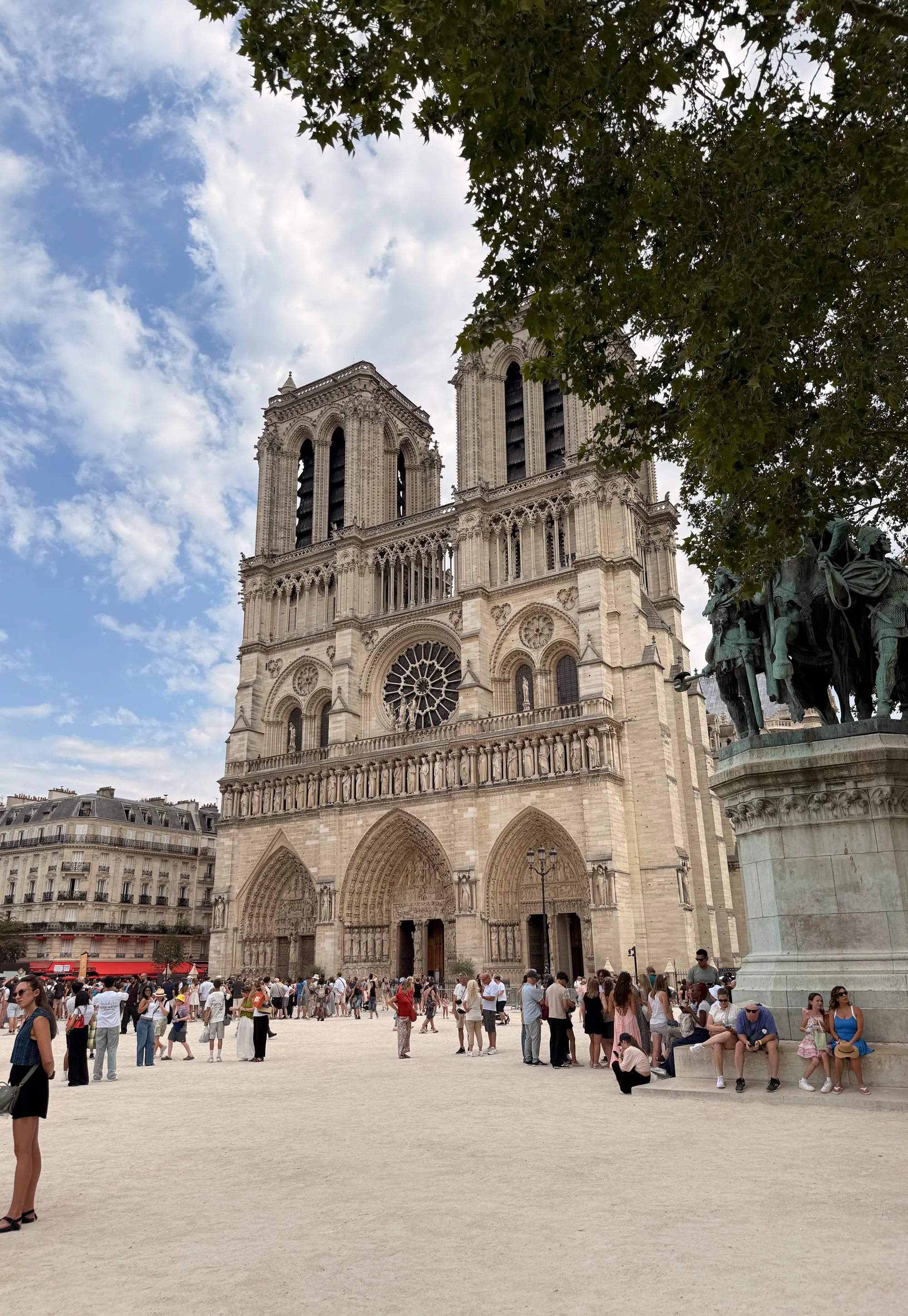 Sunny view of the west facade and twin towers of Notre-Dame in Paris with a small crowd.