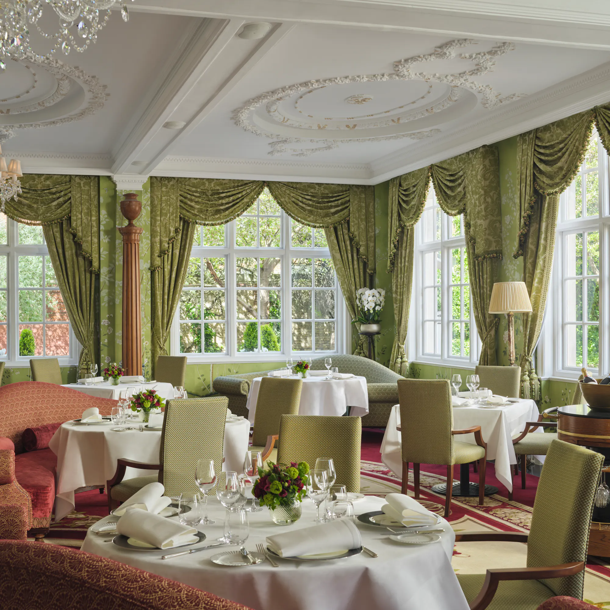 Tables set for lunch in The Goring's Dining Room, framed by sage-green drapes and garden-view windows.