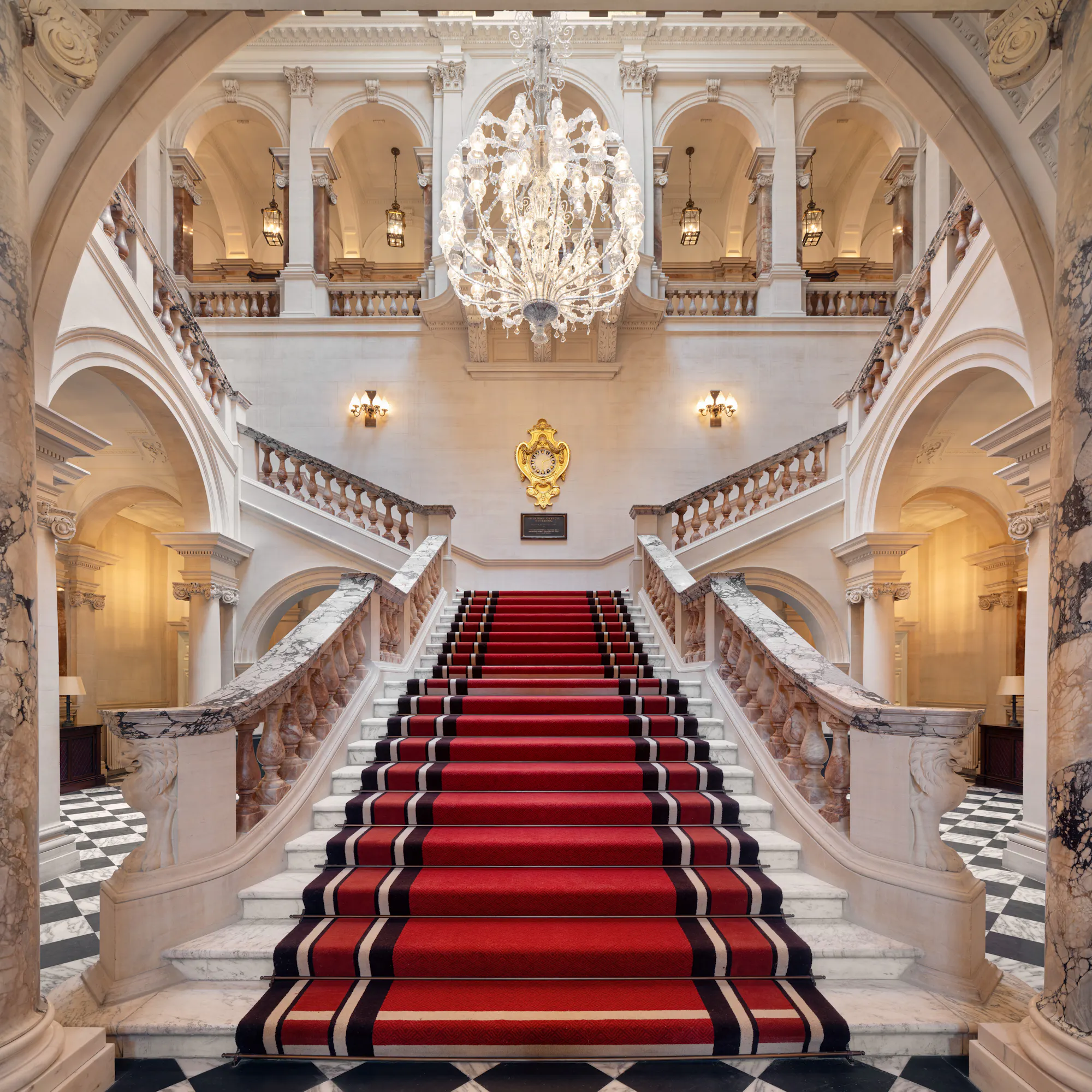 The Grand Staircase inside Raffles London at The OWO, crystal chandelier light over white marble.