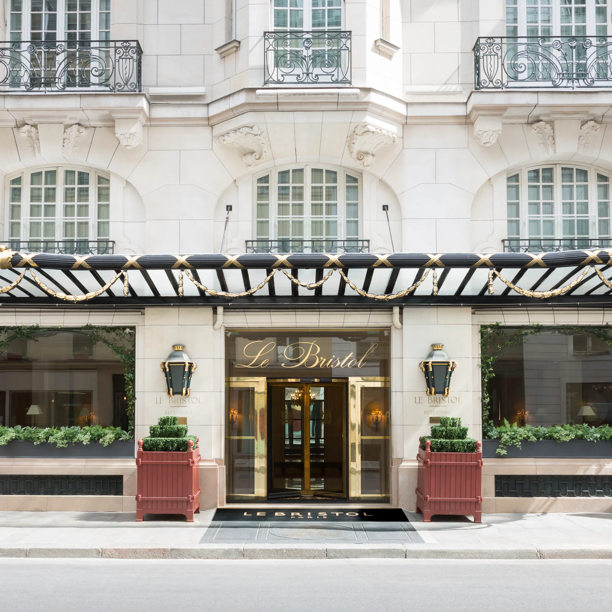 Le Bristol Paris's entrance, sun on the white stone facade and gilded doors.