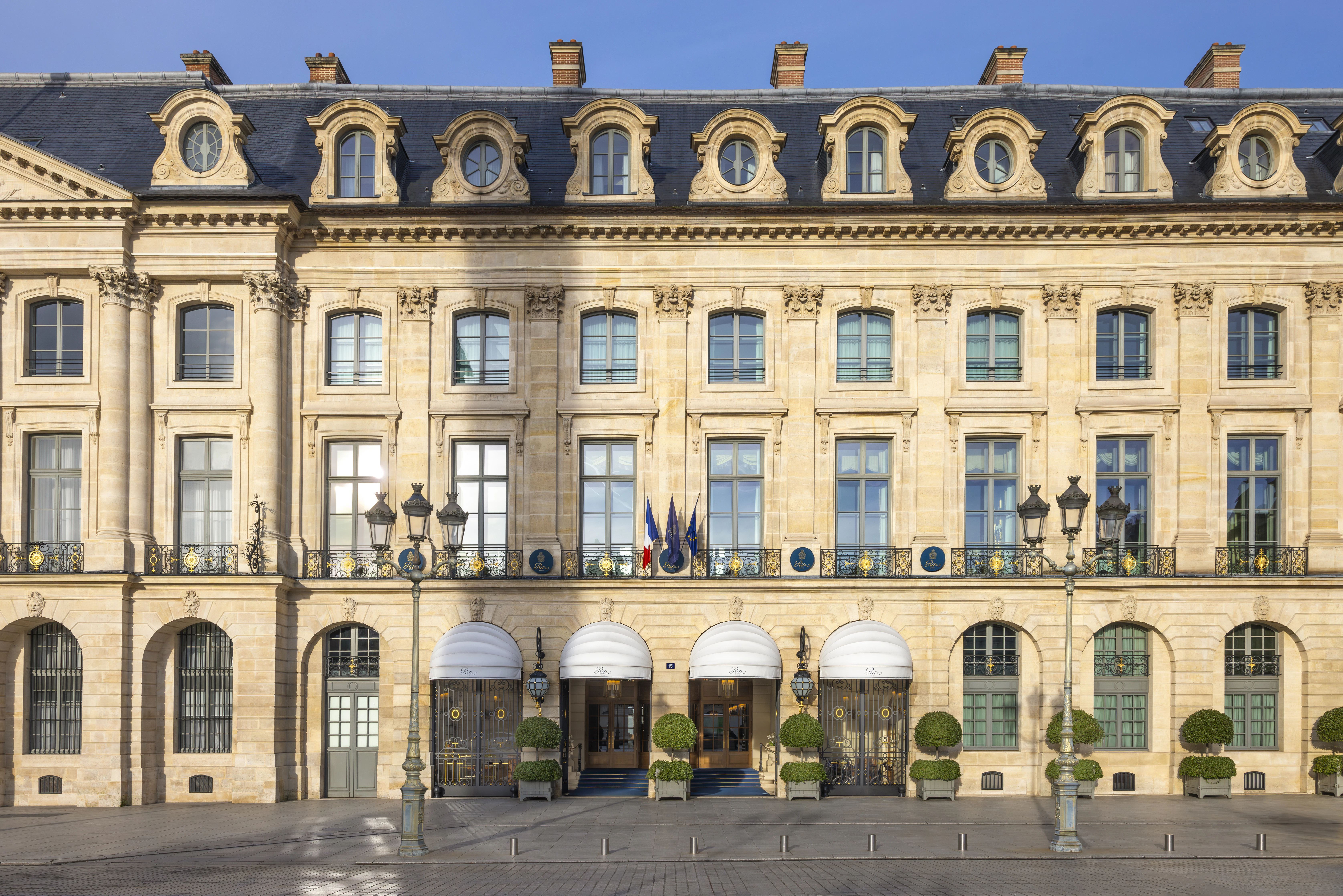 The Ritz Paris's golden stone facade on Place Vendôme, sunlight catching its mansard roof.
