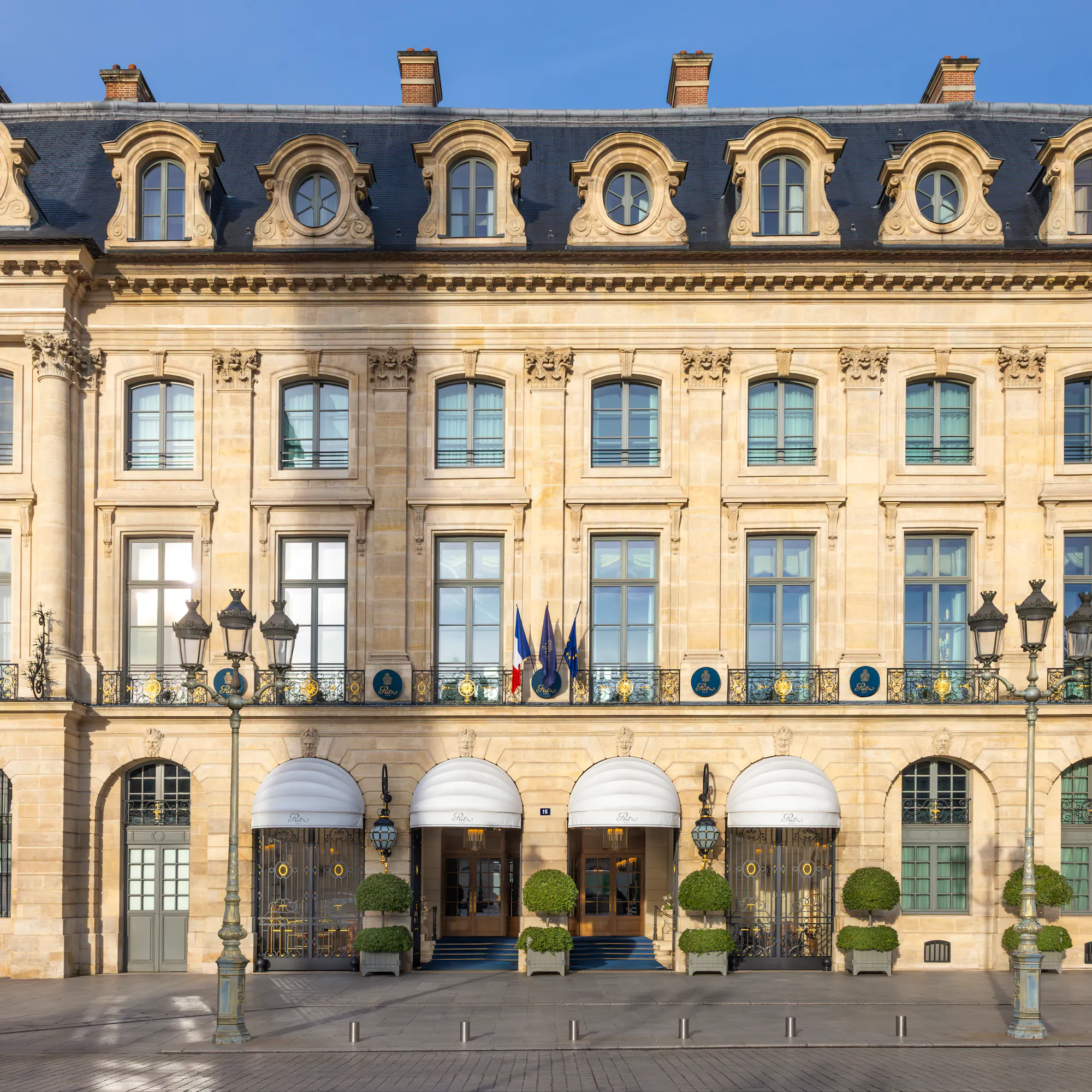 The Ritz Paris's golden stone facade on Place Vendôme, sunlight catching its mansard roof.