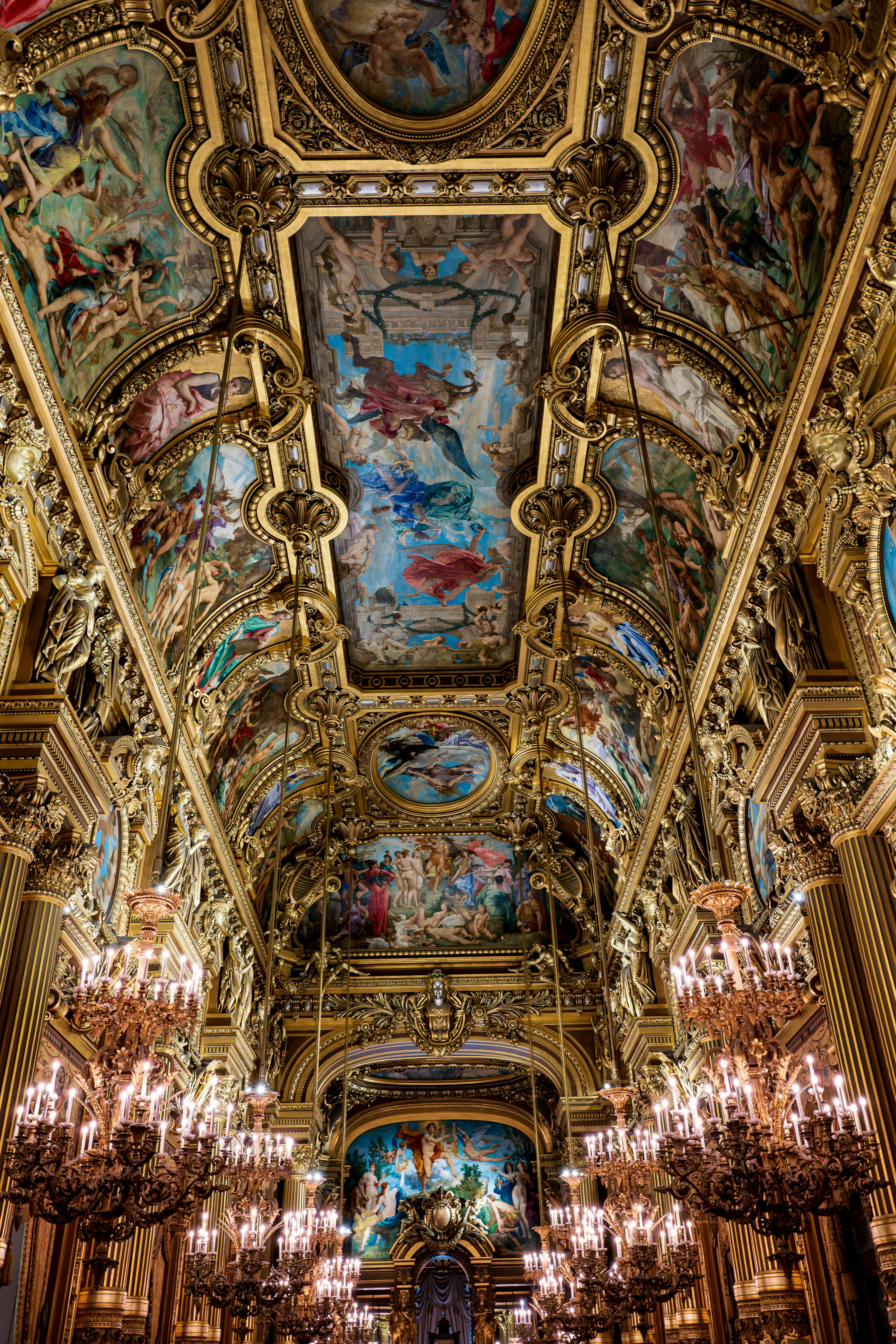 Painted ceiling of the Grand Foyer at Palais Garnier, Paris, illuminated by chandeliers.