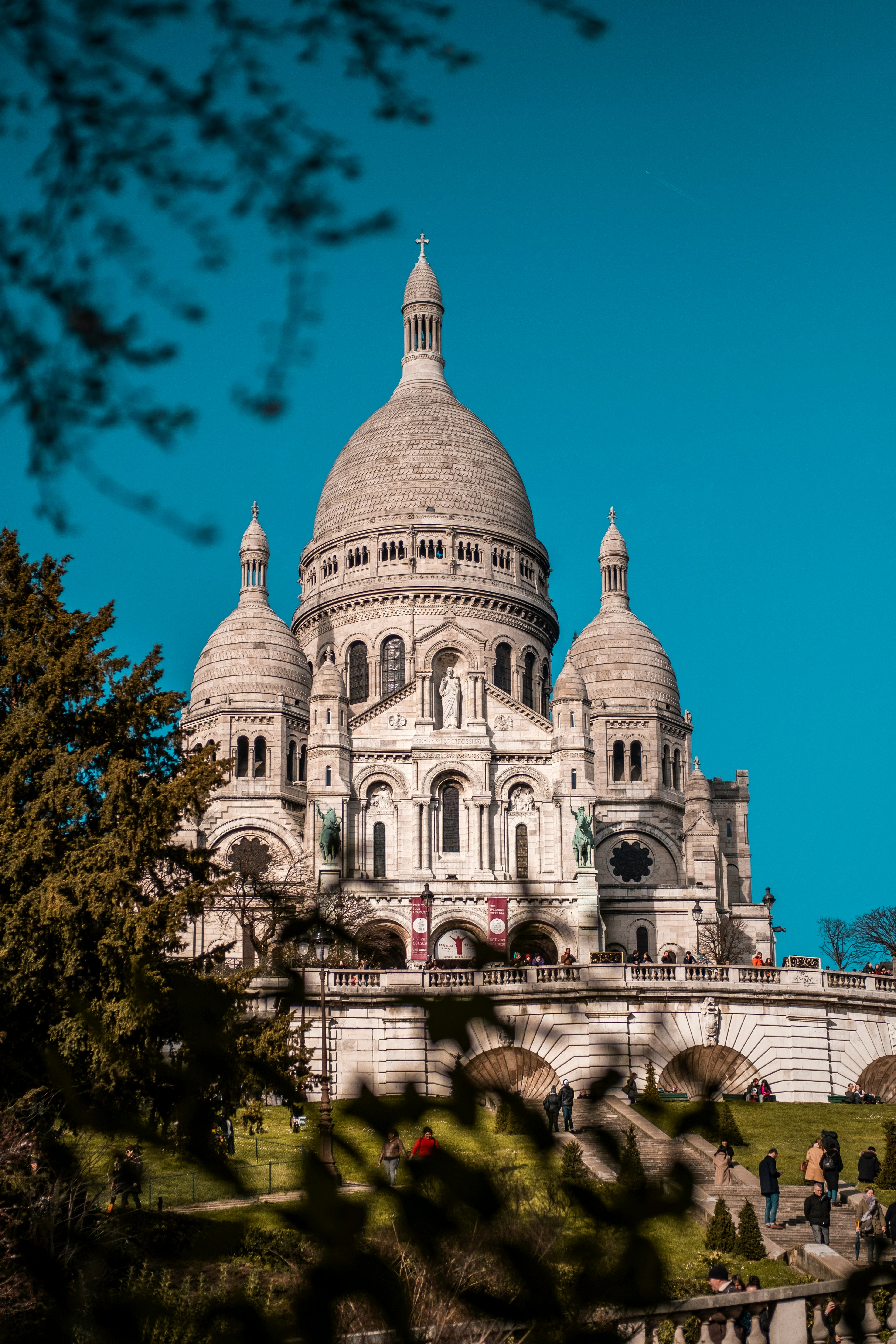 acré-Cœur's domes rising above Montmartre, framed by tree branches against a deep blue sky.