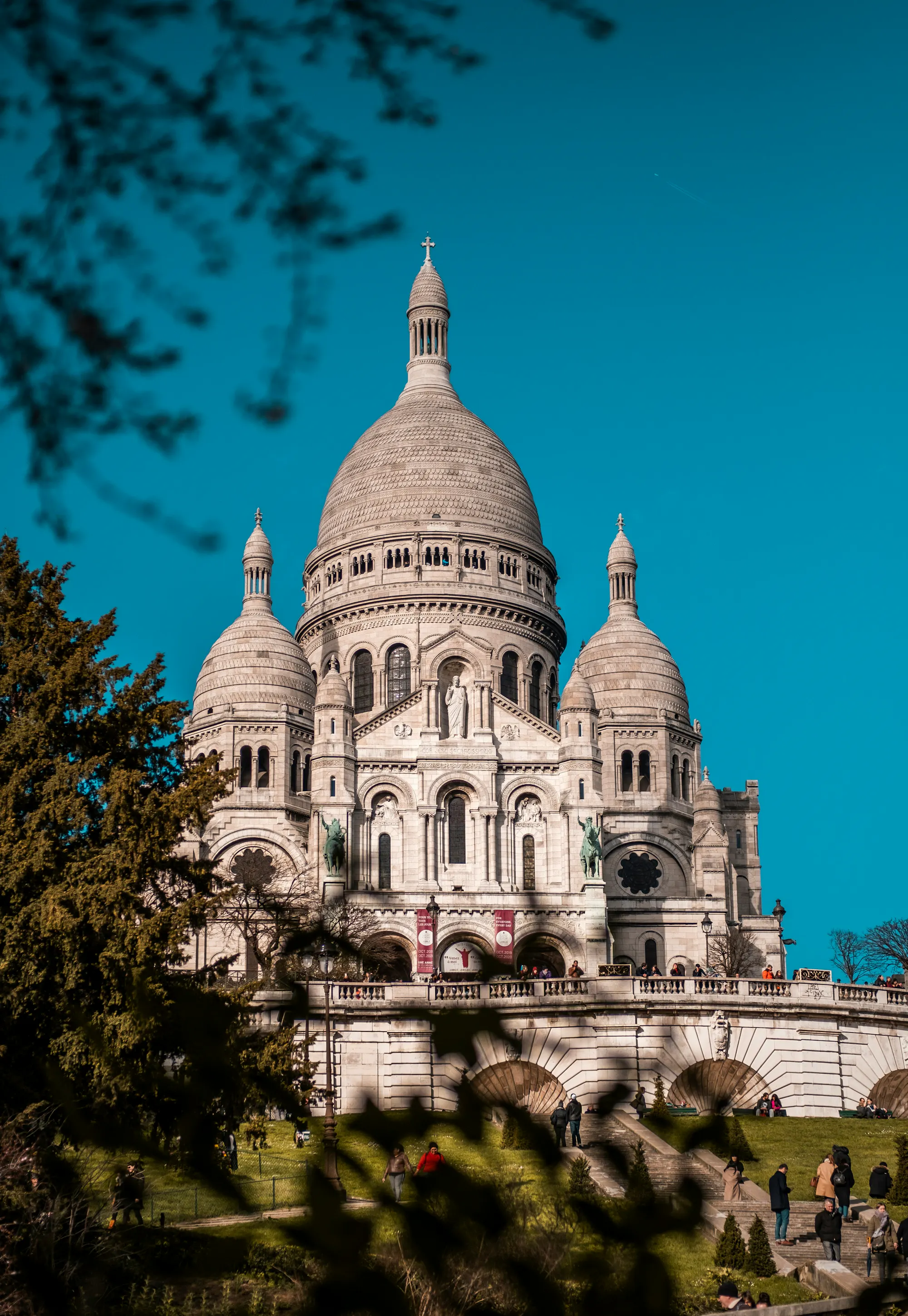 acré-Cœur's domes rising above Montmartre, framed by tree branches against a deep blue sky.