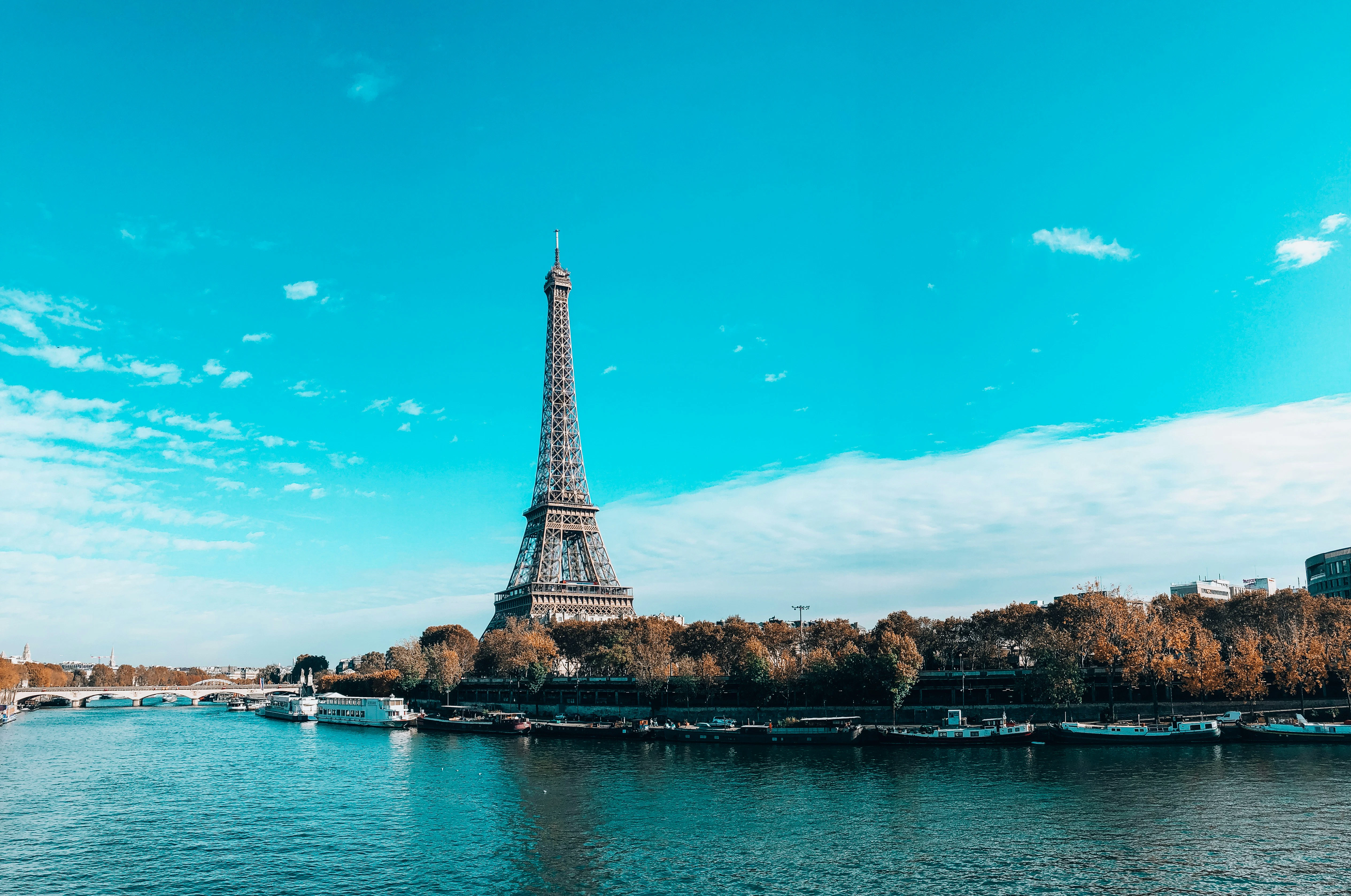 The Eiffel Tower rising above autumn trees, seen across the Seine lined with moored barges.