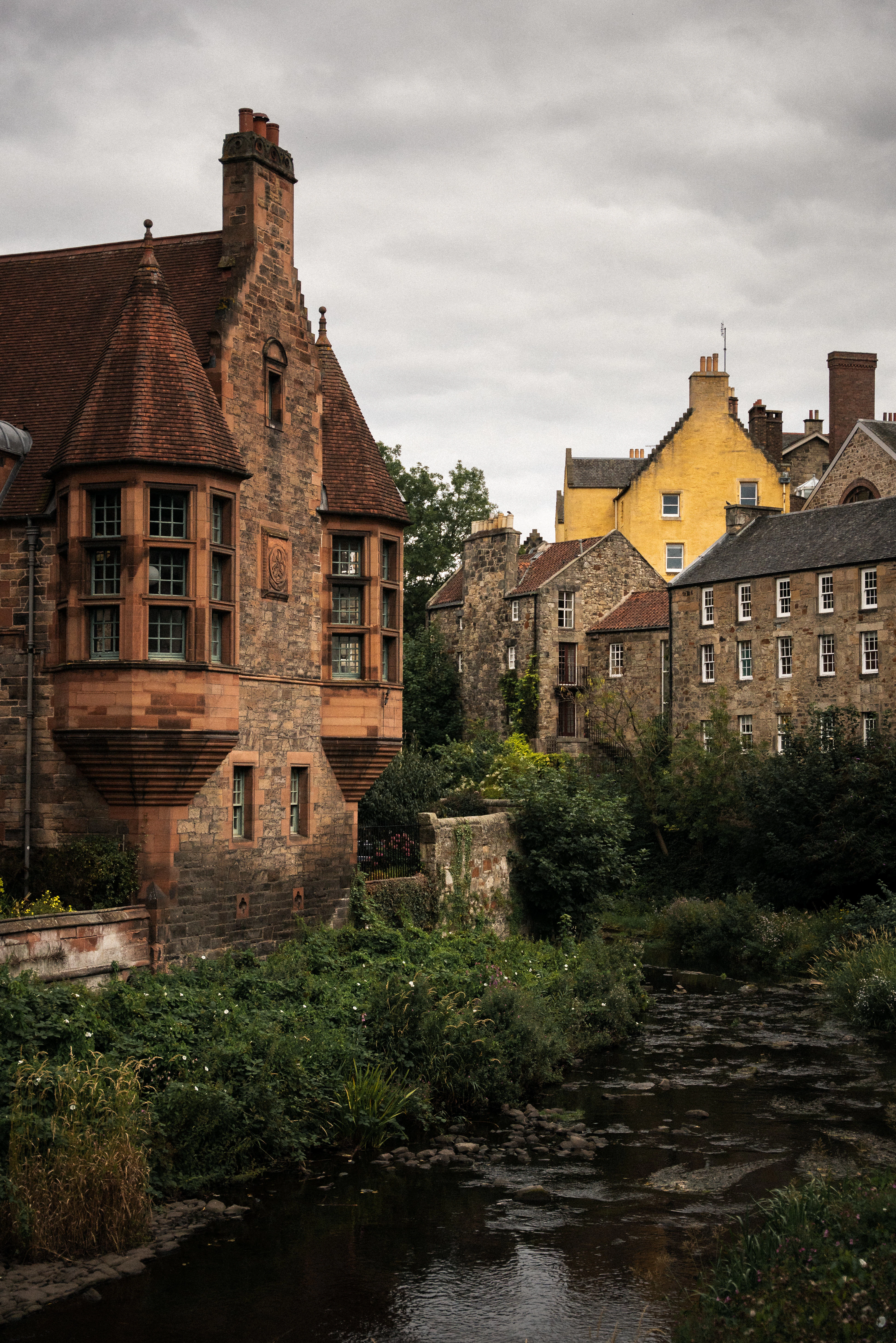 Dean Village's turreted sandstone buildings above the Water of Leith river, a yellow house behind.