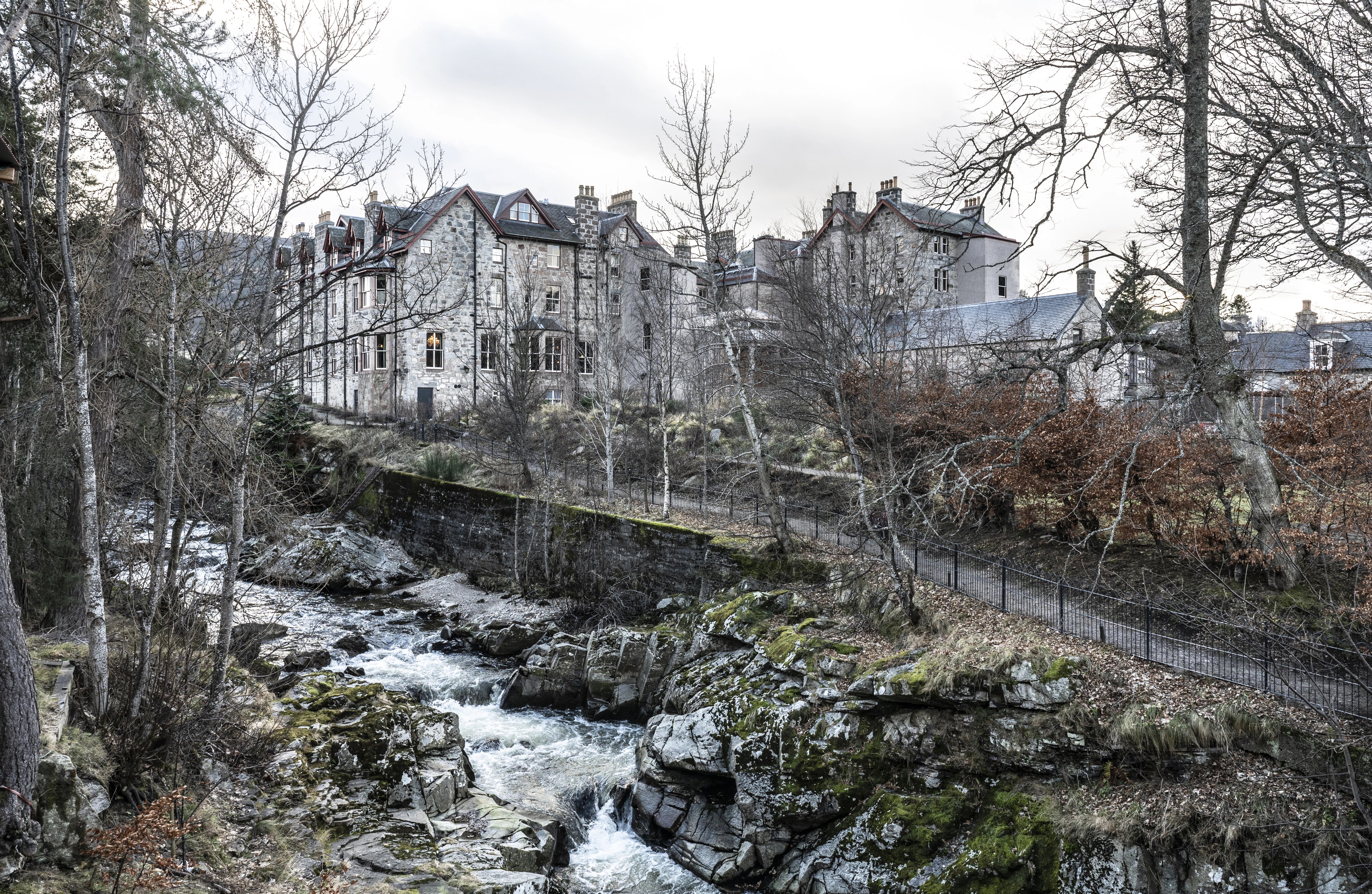 The Fife Arms hotel's stone facade above a rocky river bed, surrounded by bare winter trees.