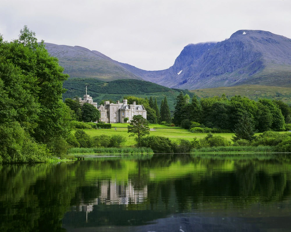Inverlochy Castle hotel reflected in a loch, with Ben Nevis in the background.