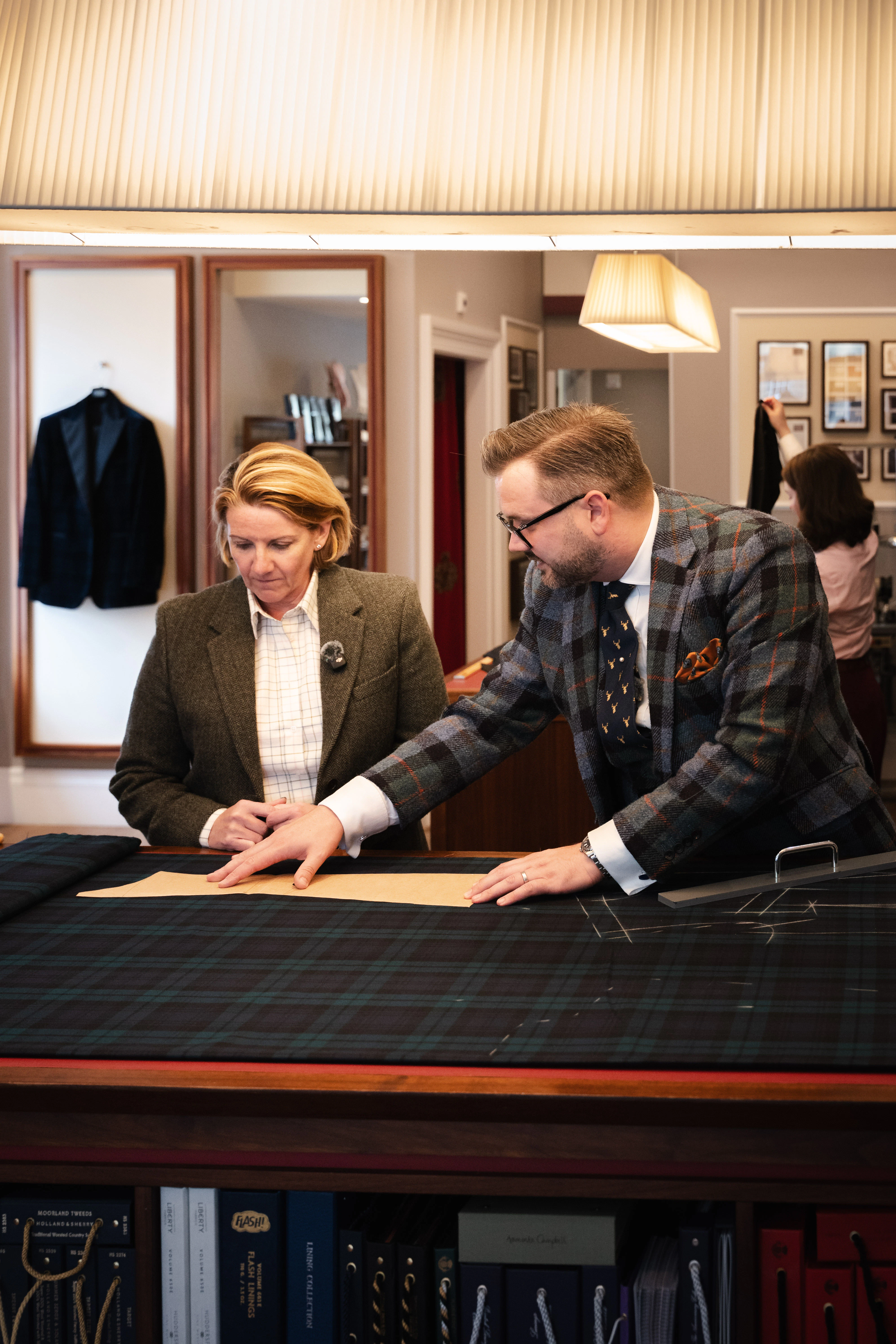 A tailor and client study a paper pattern on dark tartan cloth at Kathryn Sargent's Edinburgh shop.